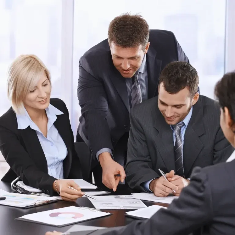 Quatre professionnels en réunion, examinant des documents autour d'une table.