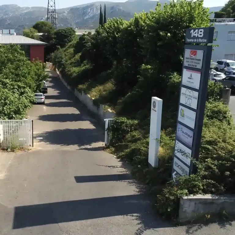 Entrée d'un chemin avec panneaux indiquant des entreprises, entourée de végétation.