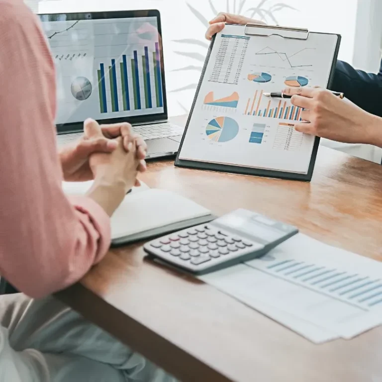 Réunion de travail avec graphiques, ordinateurs portables et calculatrice sur une table.