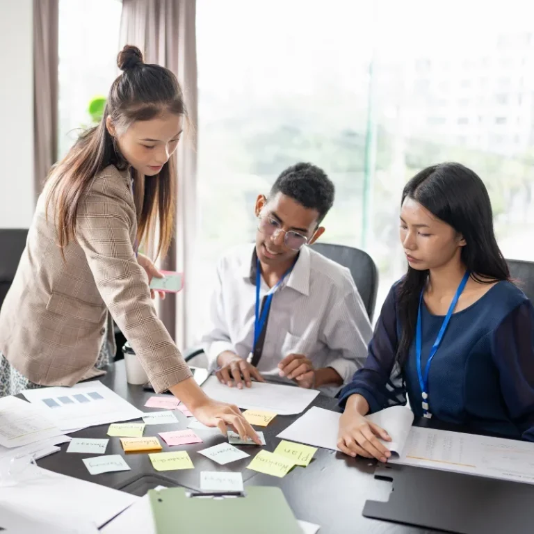Trois personnes collaborent autour d'une table, examinant des notes autocollantes.