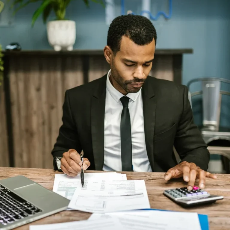 Homme en costume travaillant sur un ordinateur portable et utilisant une calculatrice.