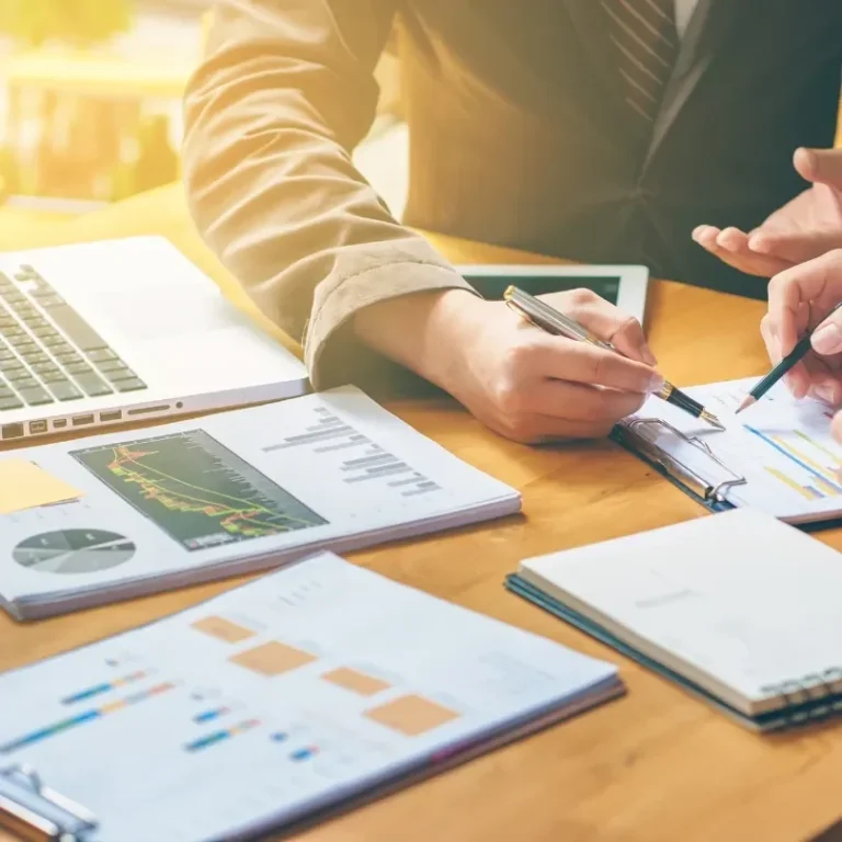 Deux personnes collaborent sur des graphiques et des documents financiers, avec un ordinateur portable.