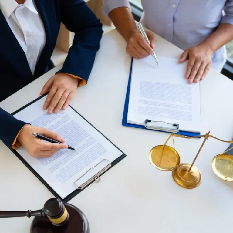 Deux personnes signent des documents juridiques sur une table avec un marteau de juge.