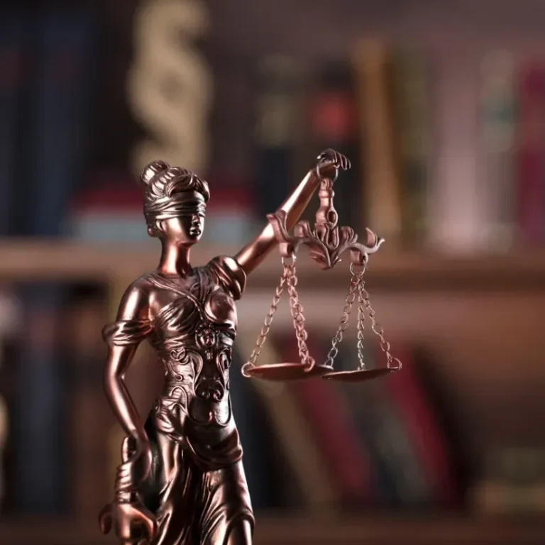 Statue de la Justice tenant des balances, avec des livres en arrière-plan.