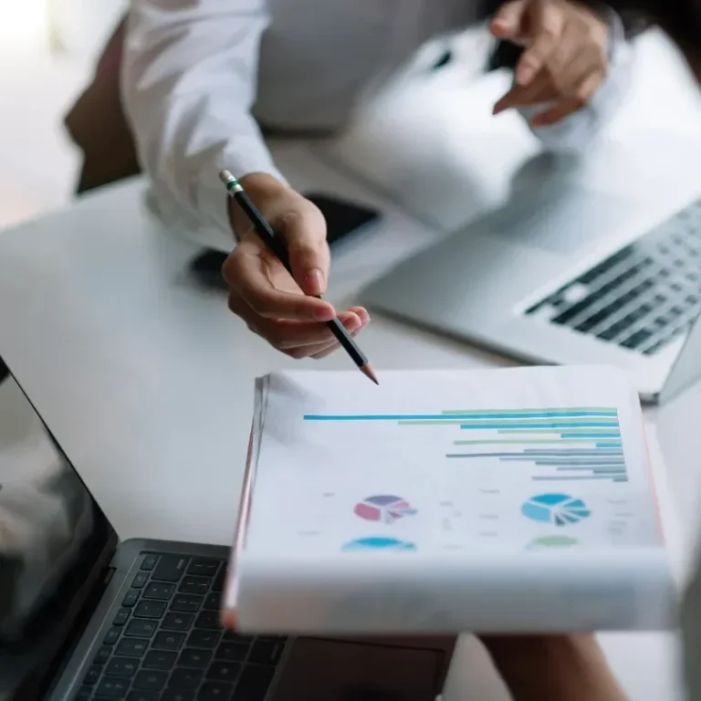 Graphs and charts on a report show data analysis, with hands gesturing and laptops nearby.