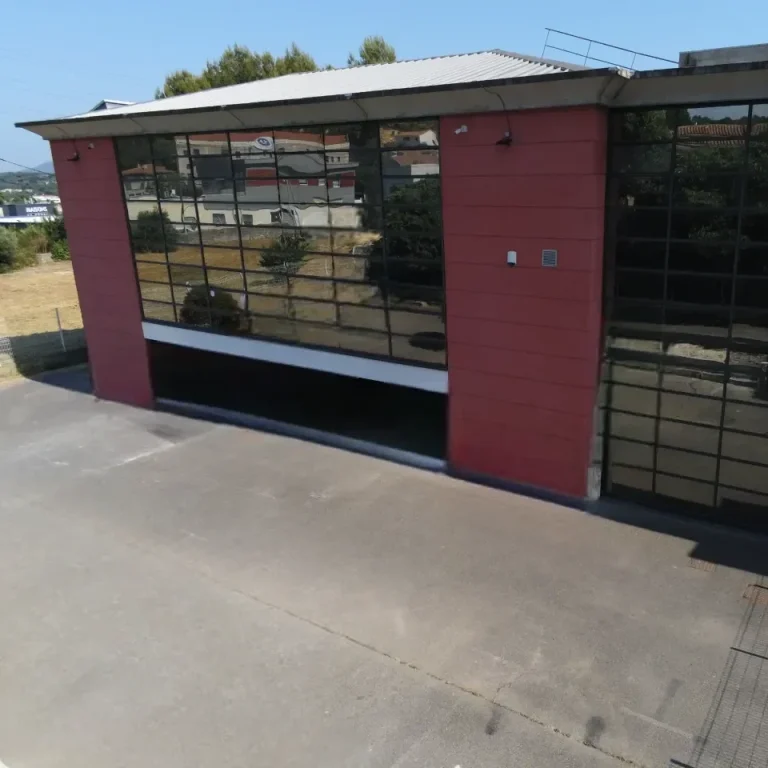 Bâtiment moderne aux murs vitrés, avec une façade rouge et un accès au niveau du sol.