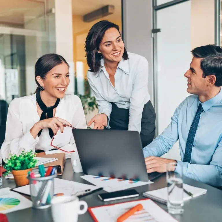 Trois professionnels discutent autour d'un ordinateur portable dans un bureau moderne.